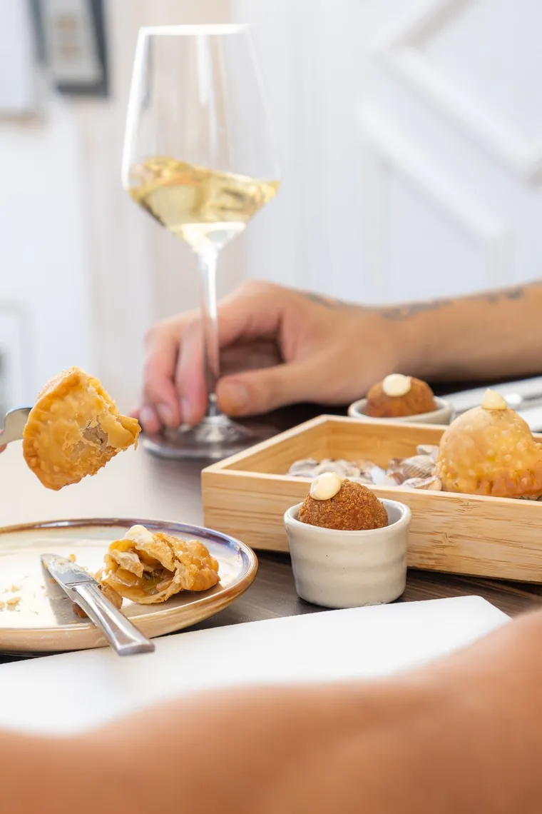 Um copo de vinho branco com o couvert do Aurora: pastéis de berbigão e bolinhas de leitão